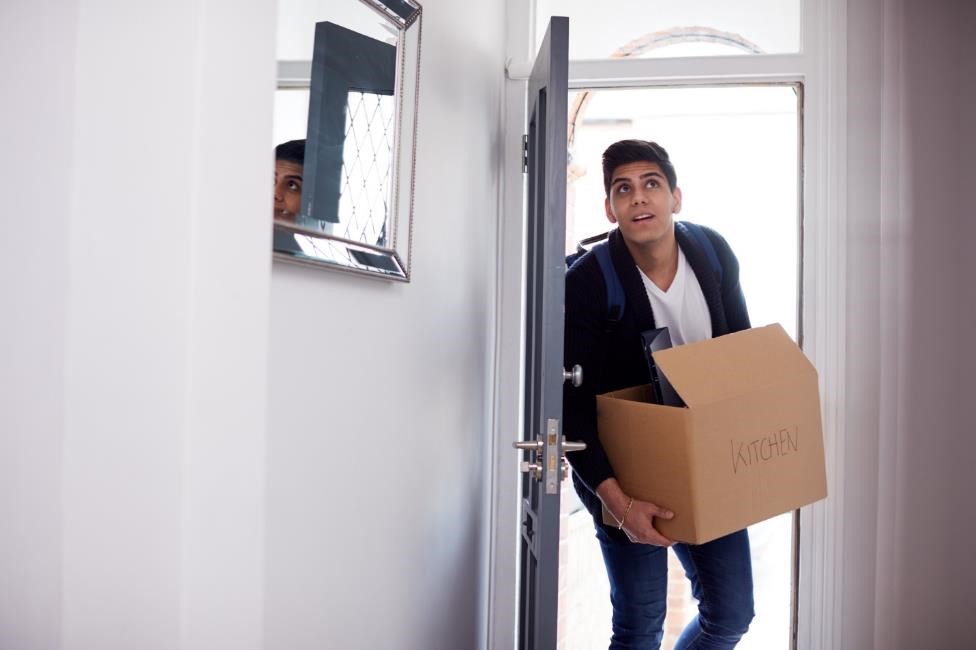 College student walking through a door carrying a moving box.