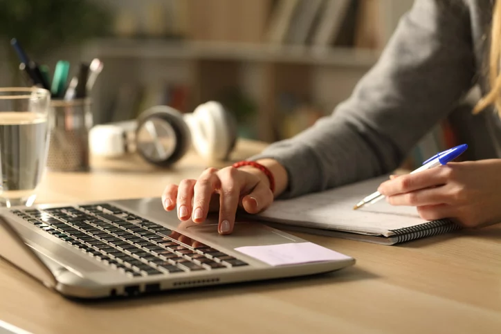 Person searching on a computer next to a notepad.