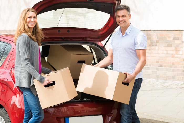 middle-aged couple loading moving boxes into red car