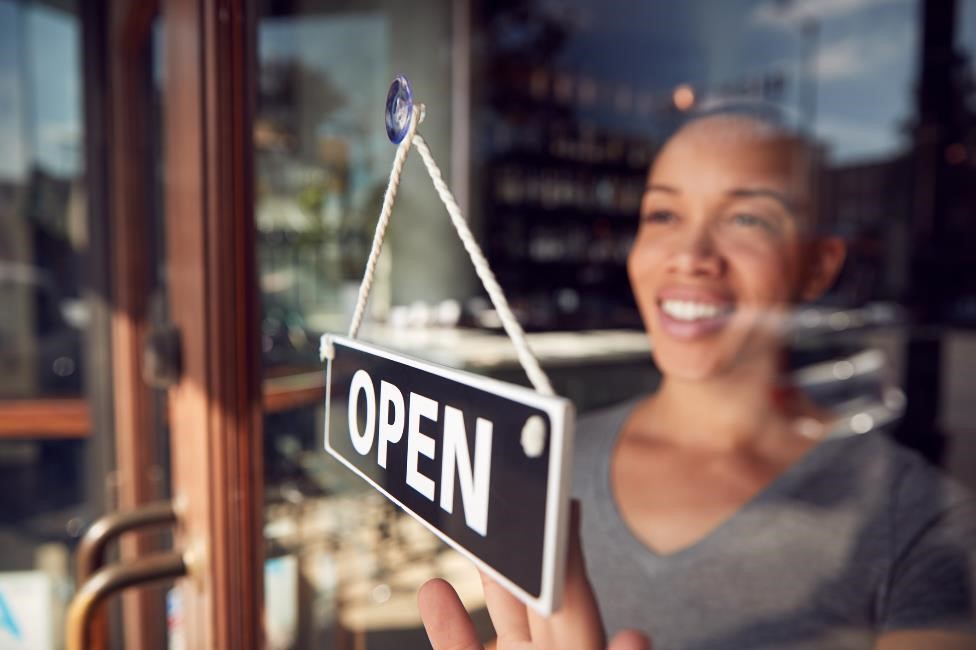 woman turning a business's window sign from open to closed