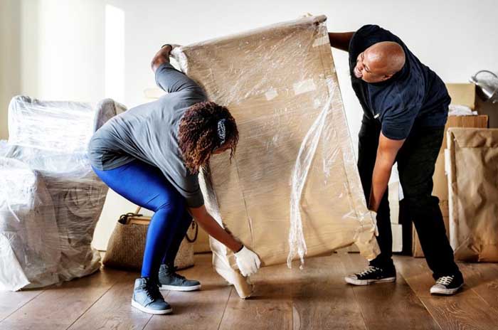 two people wrapping furniture in plastic to prep for moving