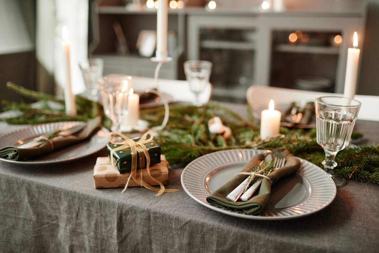 Dishes and place settings are arranged on a table next to small gifts and festive greenery