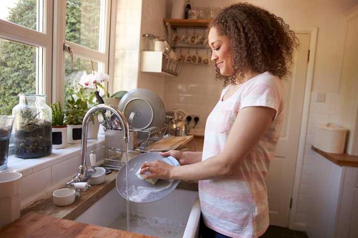 a Black woman washing dishes at the sink