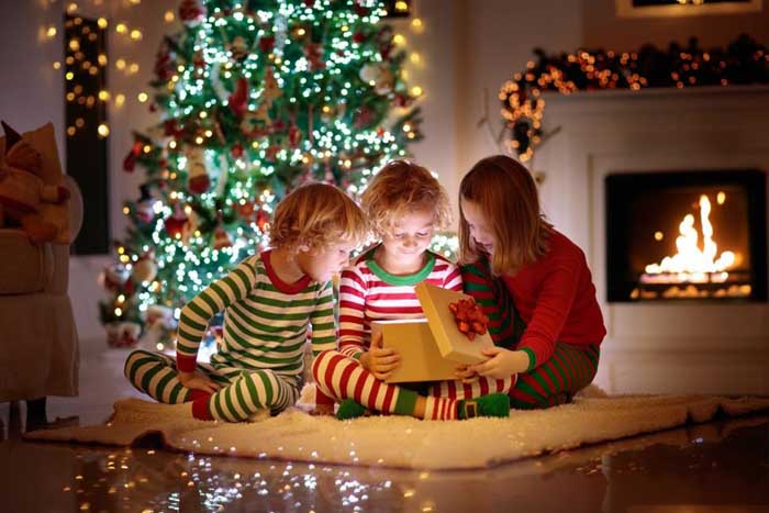 three children sitting in front of a Christmas tree opening gifts