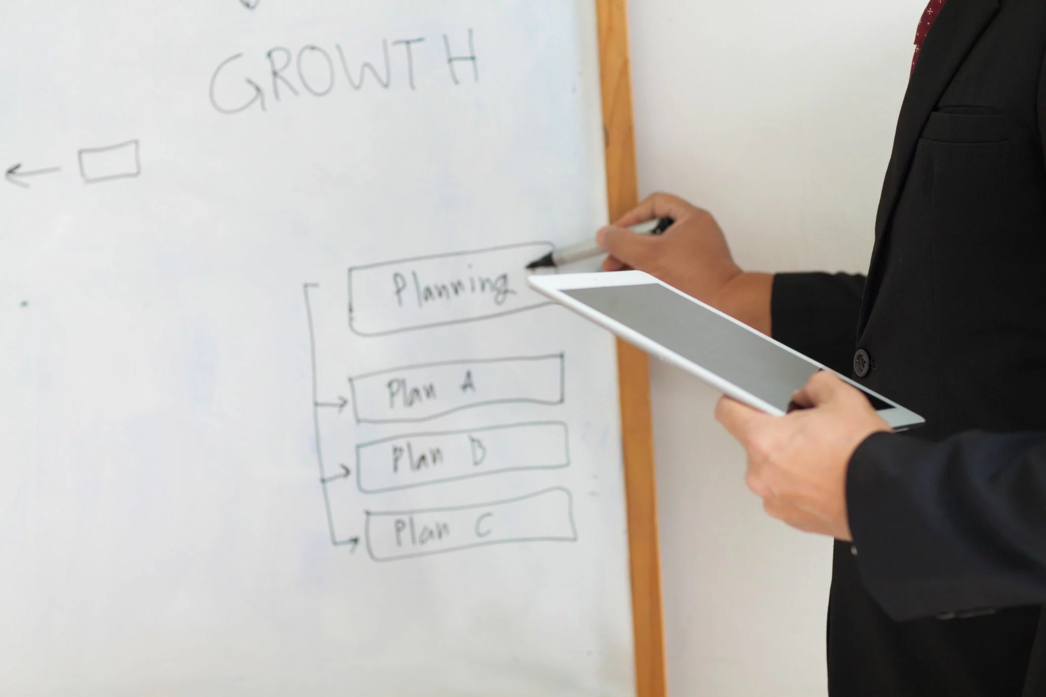 A person holds a tablet and writes about planning on a whiteboard on the wall