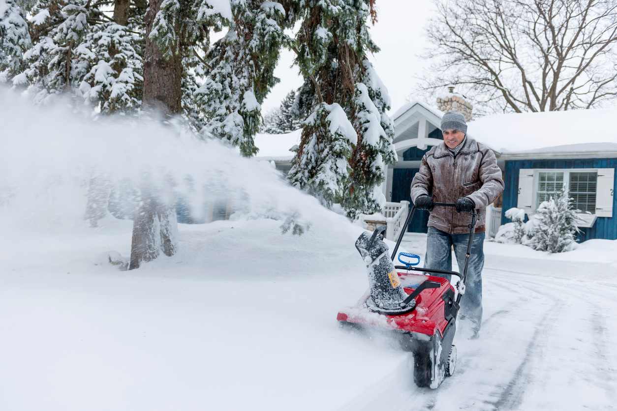 A man clears a driveway covered in snow using a red snow blower