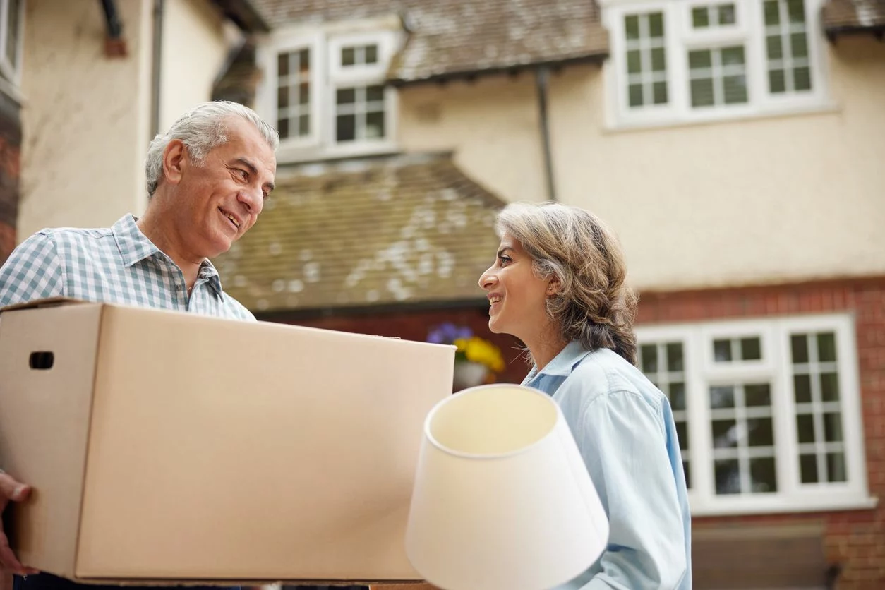 An older couple carries things out of their home while downsizing