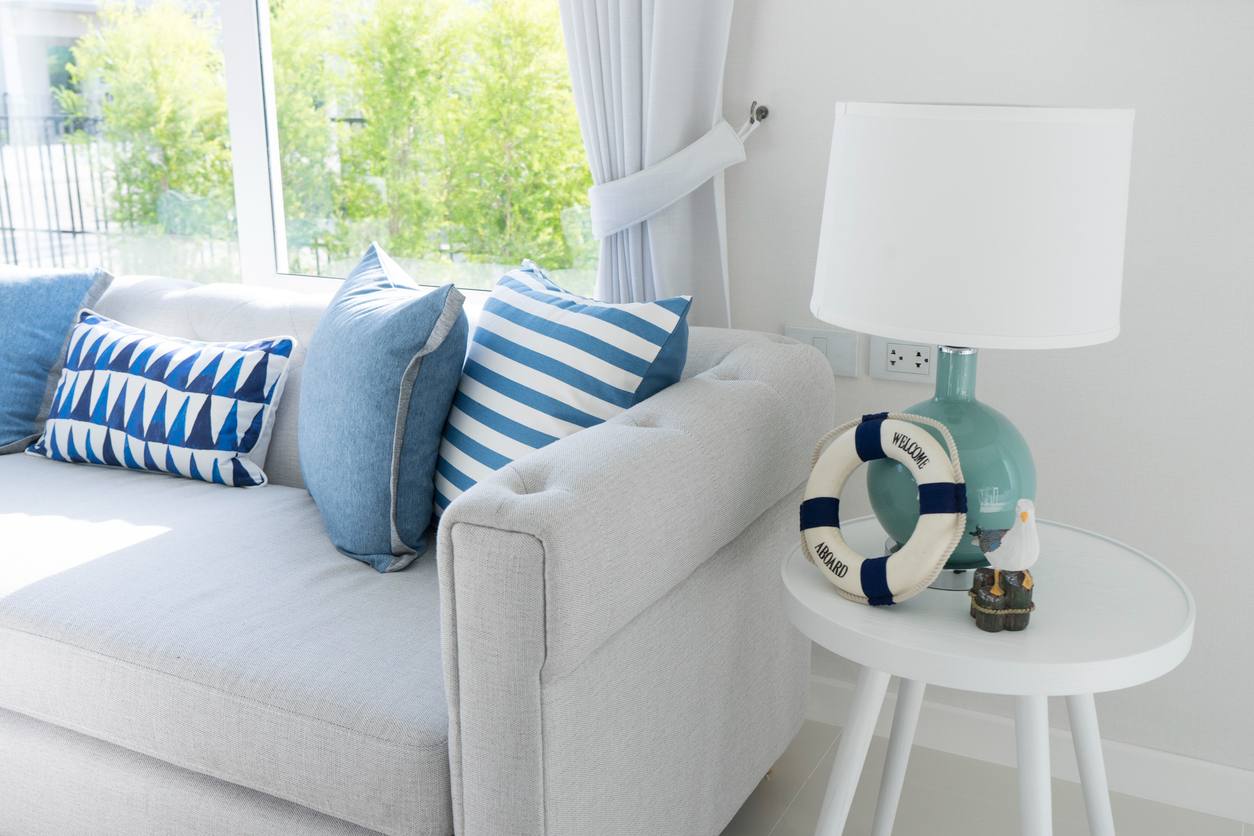 Living room decorated for vacation rental with a cozy, large white couch, white side table and throw pillows in a variety of shades of blue.