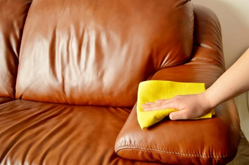 A person cleaning a leather sofa with a microfiber cloth