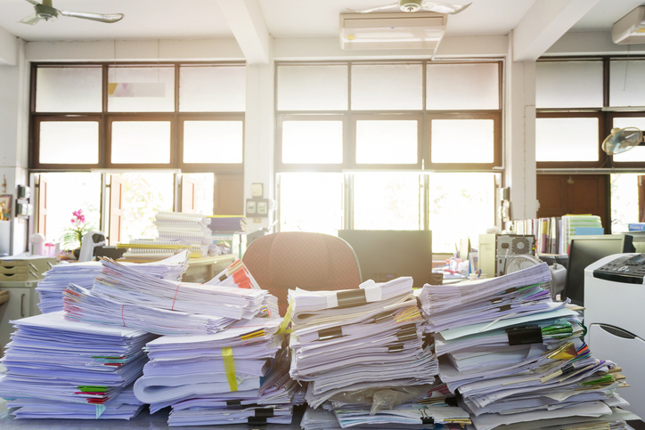Several stacks of paper documents and files on a messy desk.