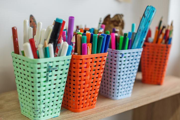 Pens, pencils, and other school supplies resting in colorful cups.