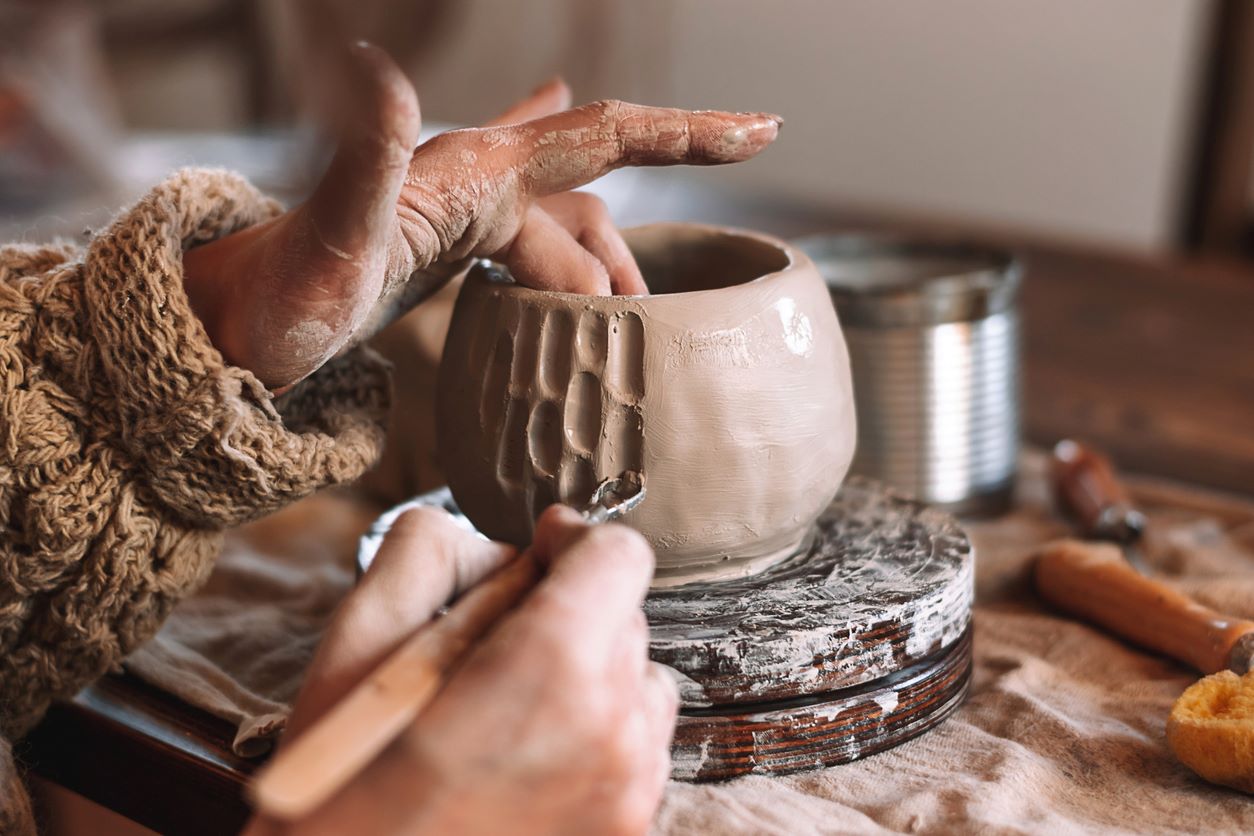 A woman etches into a clay bowl while working on her pottery.