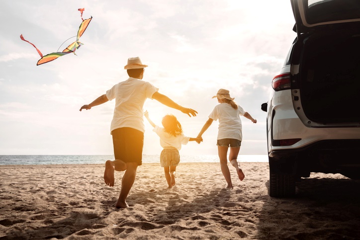 A happy family runs onto the beach after planning a road trip along the coast.