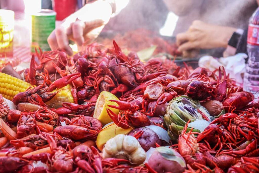 Boiled crawfish and vegetables piled on red checkered tablecloth outdoors.