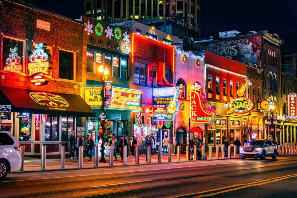 Illuminated neon signs on storefronts along the street in Downtown Nashville.