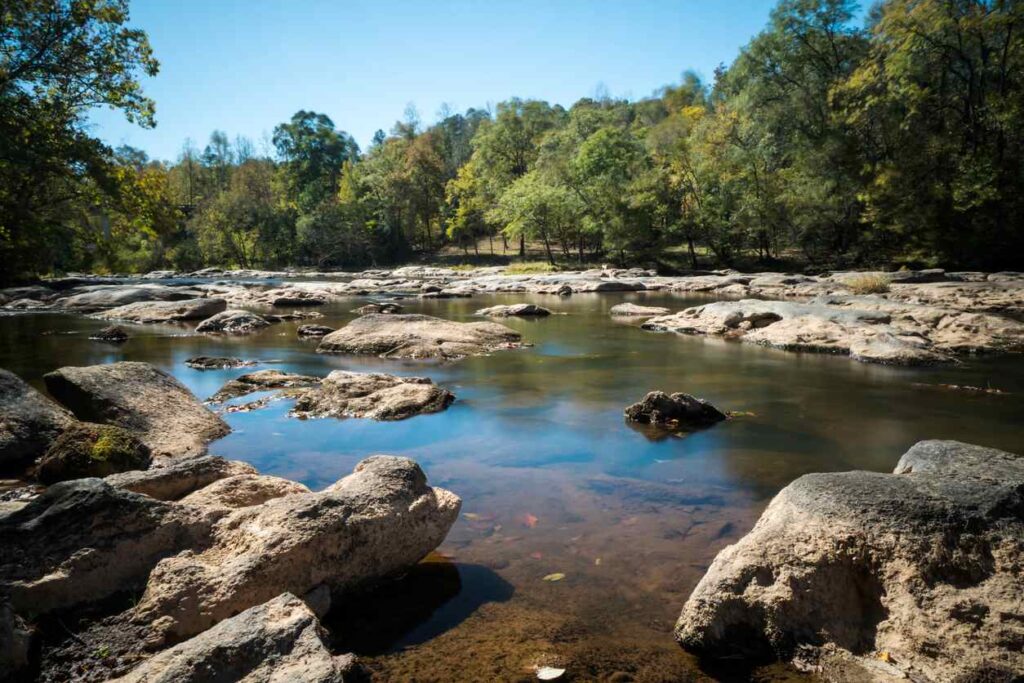 A beautiful, rocky river outside of Spartanburg is surrounded by leafy trees.