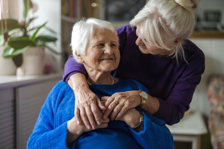 A woman smiles as she hugs her mother in her senior living home.