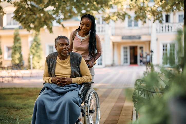 A woman pushes her father’s wheelchair as she visits him in assisted living.