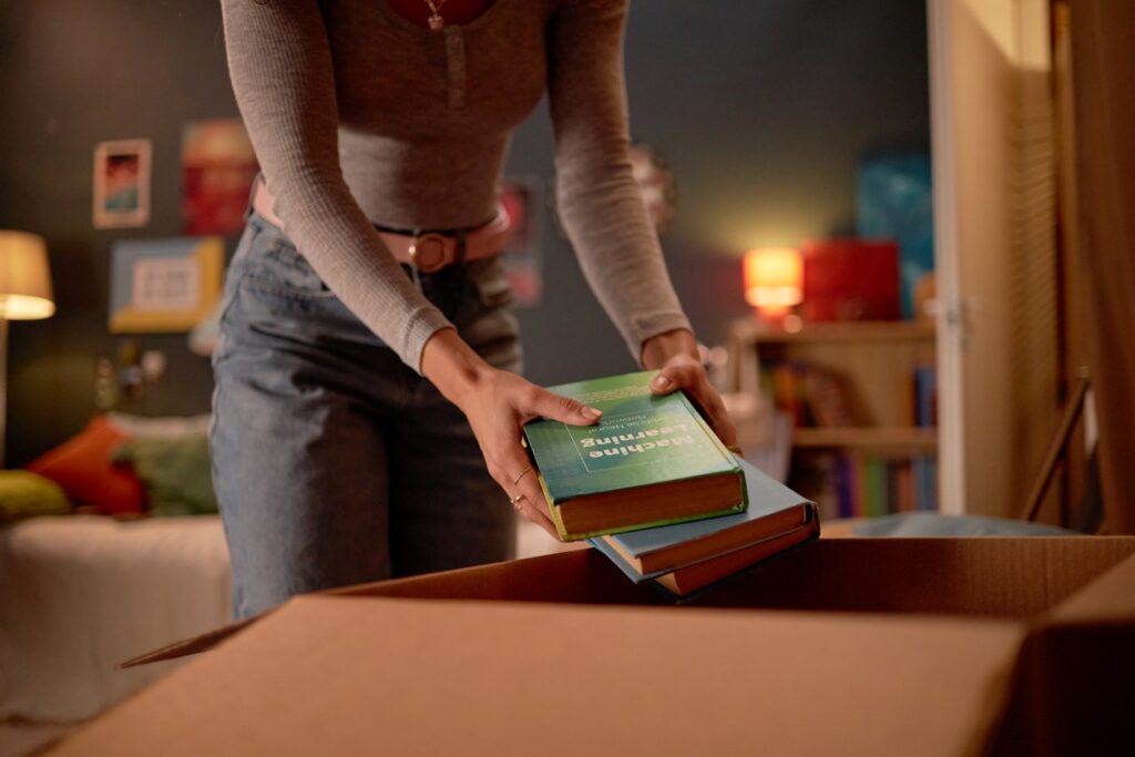 A college graduate places textbooks in a box while packing up her home.