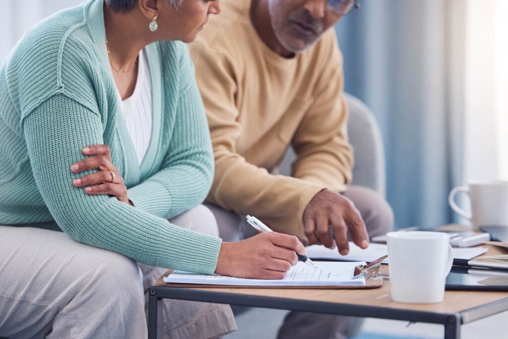 A couple sits together on the couch, working on paperwork with coffee mugs on the table.