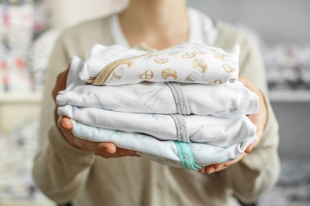 A woman holds a stack of folded onesies before placing them into infant clothing storage. 