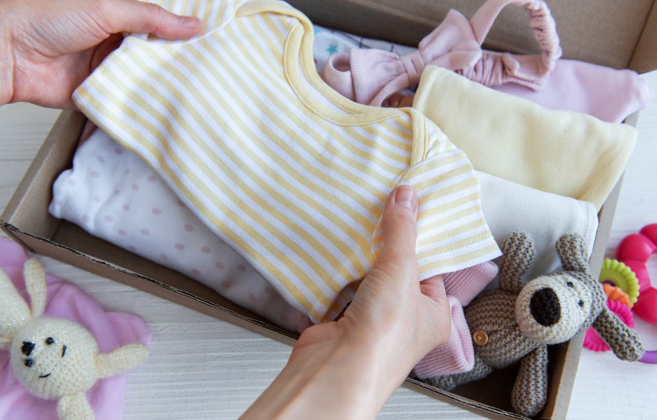 A woman packs a yellow-and-white-striped onesie into a baby clothes organizer with other baby clothes and toys.