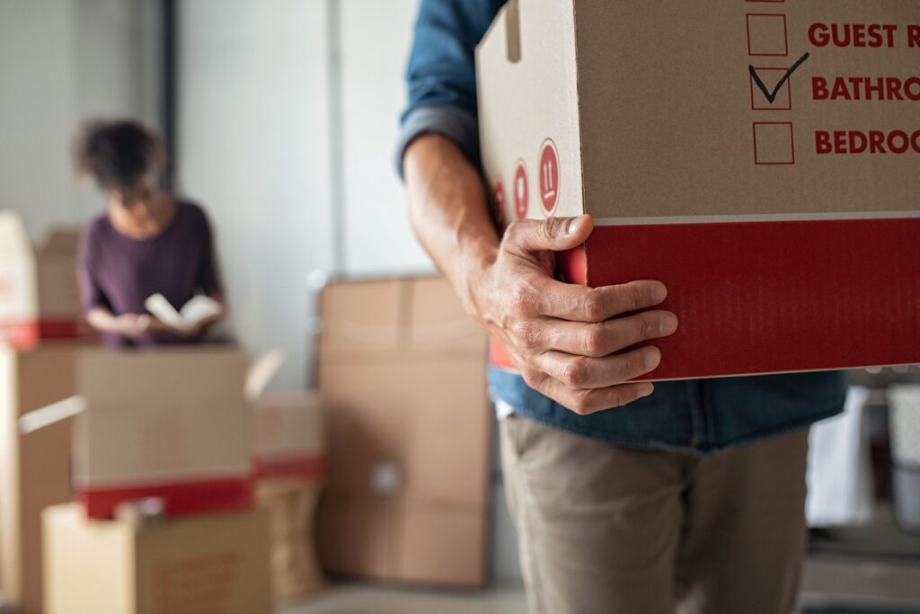 A man holds a box of packed items next to a woman packing other boxes while moving.